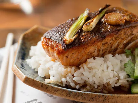 Crispy-skinned soy-glazed salmon fillet over white rice with charred scallions, cucumber and cilantro on a ceramic plate at Myers + Chang in Boston