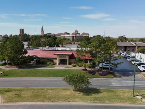 Exterior of Grand House Asian Bistro at 2701 N Classen Blvd in Oklahoma City, a red-roofed building with signage and parking lot, with the OKC skyline behind it