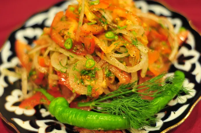 Achichuk-style tomato and onion salad garnished with dill and a green chili on a traditional patterned plate at Cafe Kashkar