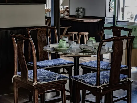 Interior of Sichuan Alley Bistro in West Hartford with a marble-topped table, carved wooden chairs with blue cushions, and the restaurant's branded host stand
