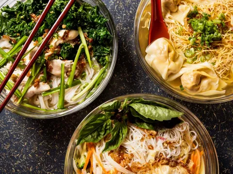 Three glass bowls of soup and noodles at Rainbow Chinese in Minneapolis — a chicken rice-noodle soup with kale and chopsticks, a wonton egg-noodle soup, and a basil-topped rice-noodle bowl